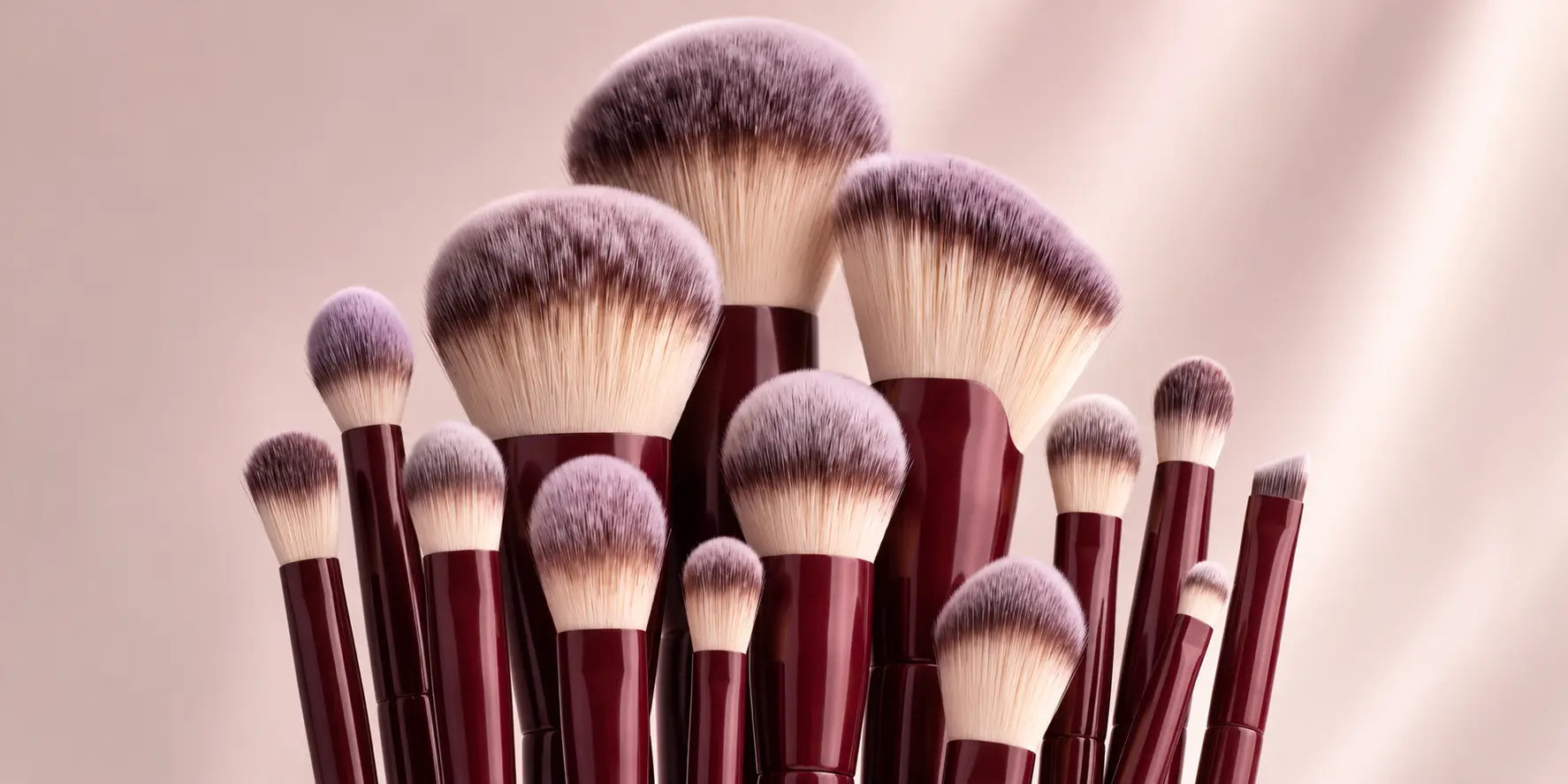 Wijnrode make-up kwasten tegen een roze achtergrond, sfeerbeeld bij de Flawless keuzehulp